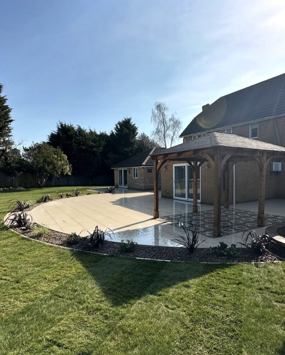 Curved cream porcelain patio around a house with a timber gazebo and gravel planting margin
