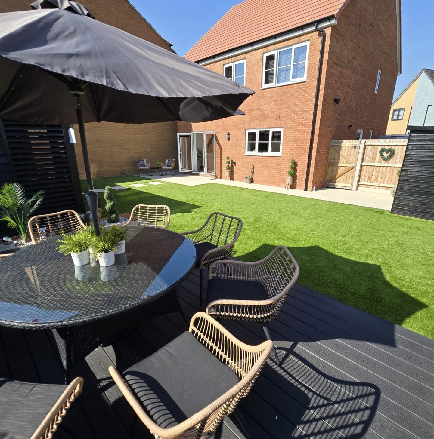 Composite deck with dining furniture and a parasol overlooking an artificial grass lawn