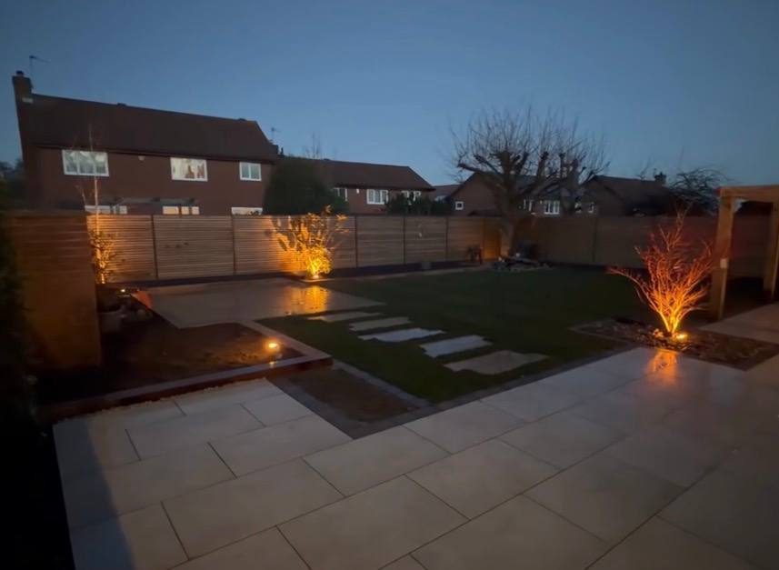 Garden at dusk with uplit shrubs and lit stepping stones