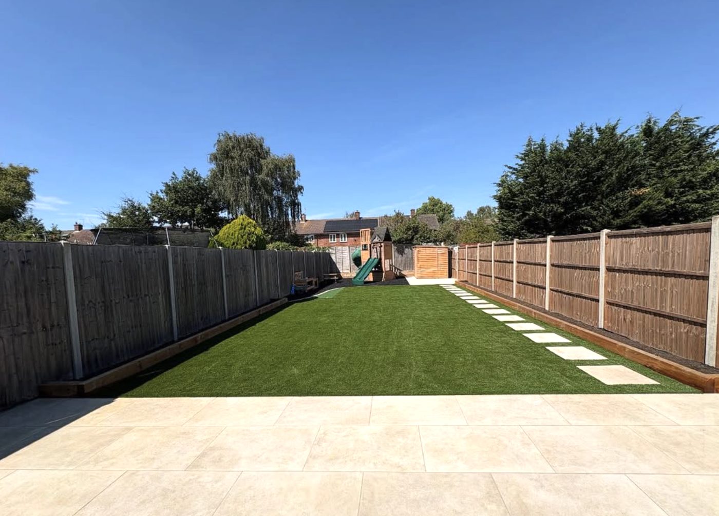 Long garden with artificial grass, stepping stones and a large porcelain patio