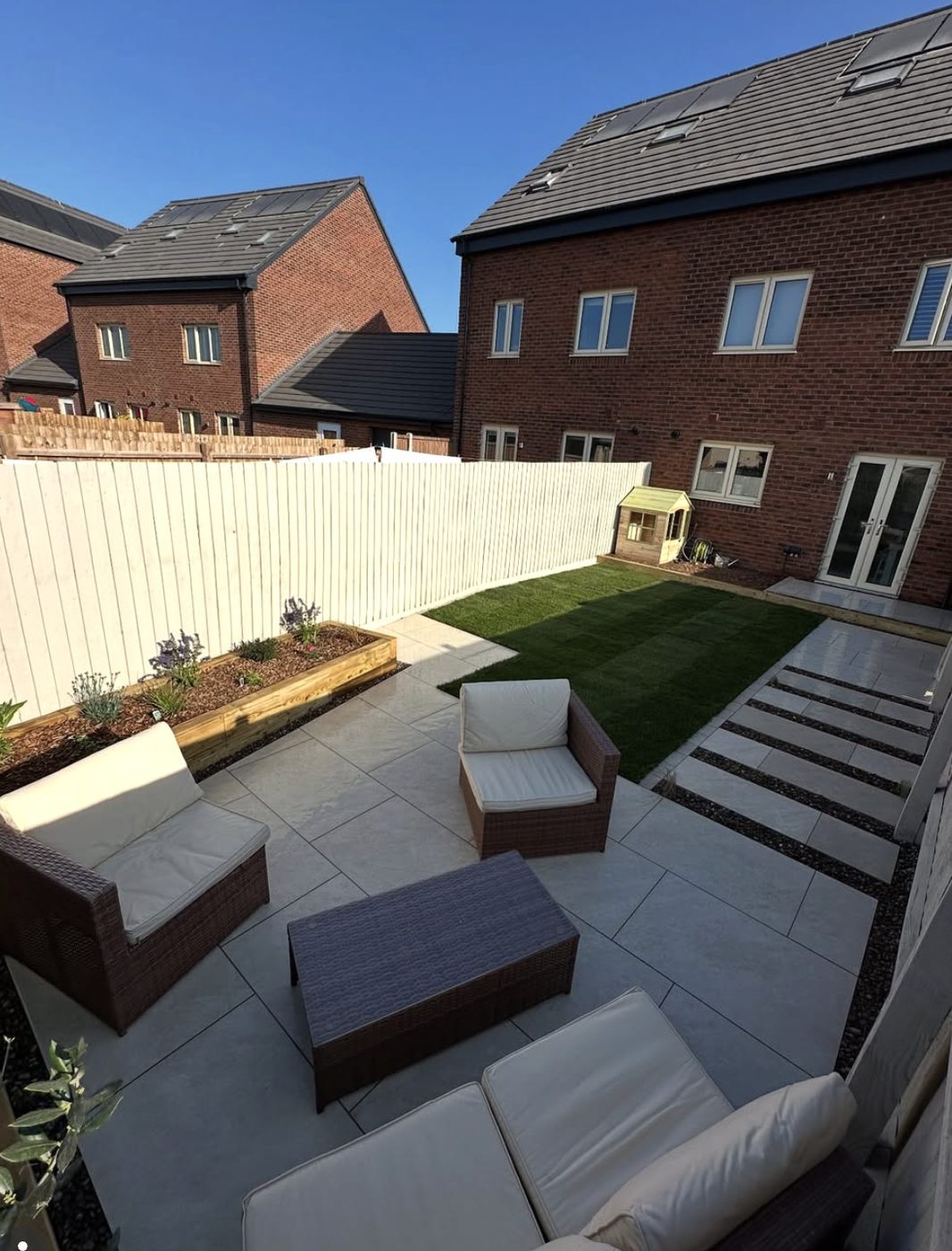 Grey porcelain patio with outdoor sofas, a sleeper raised bed and stepping stones through a lawn
