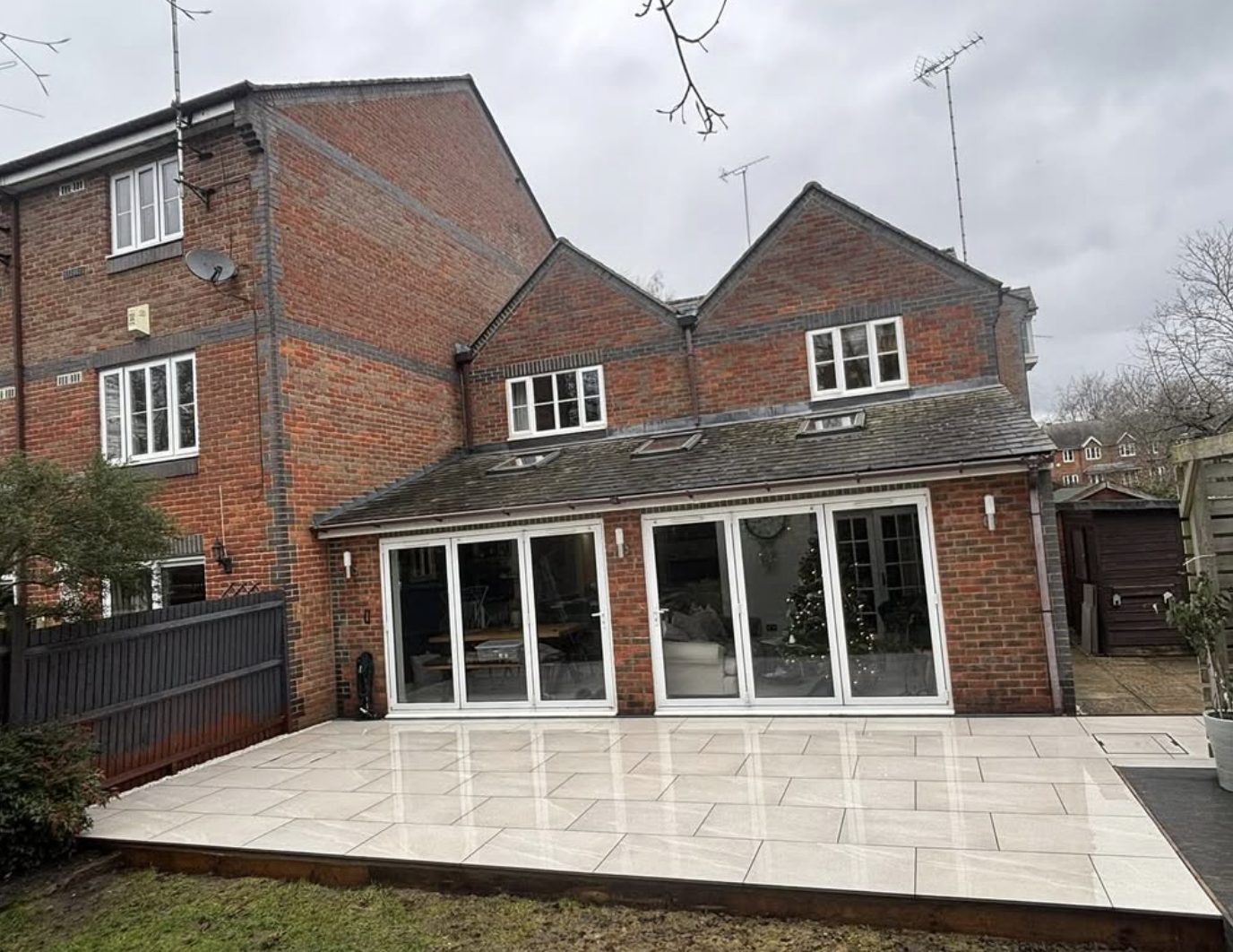 Large light porcelain patio across the back of a brick house with bifold doors