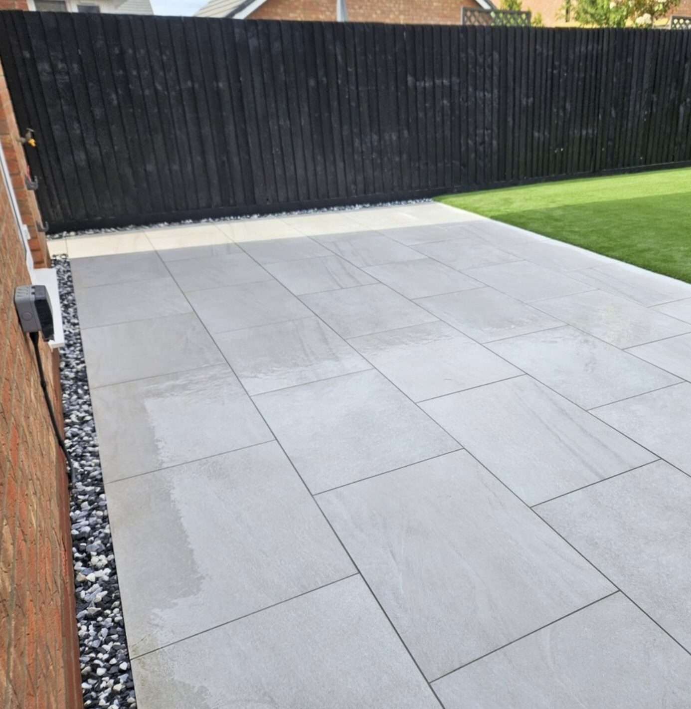 Grey porcelain patio with a pebble margin along the house wall