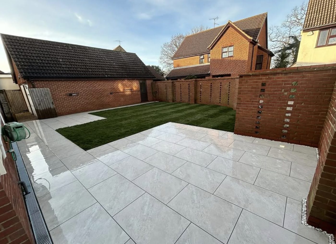 Light porcelain patio and freshly laid turf enclosed by brick walls
