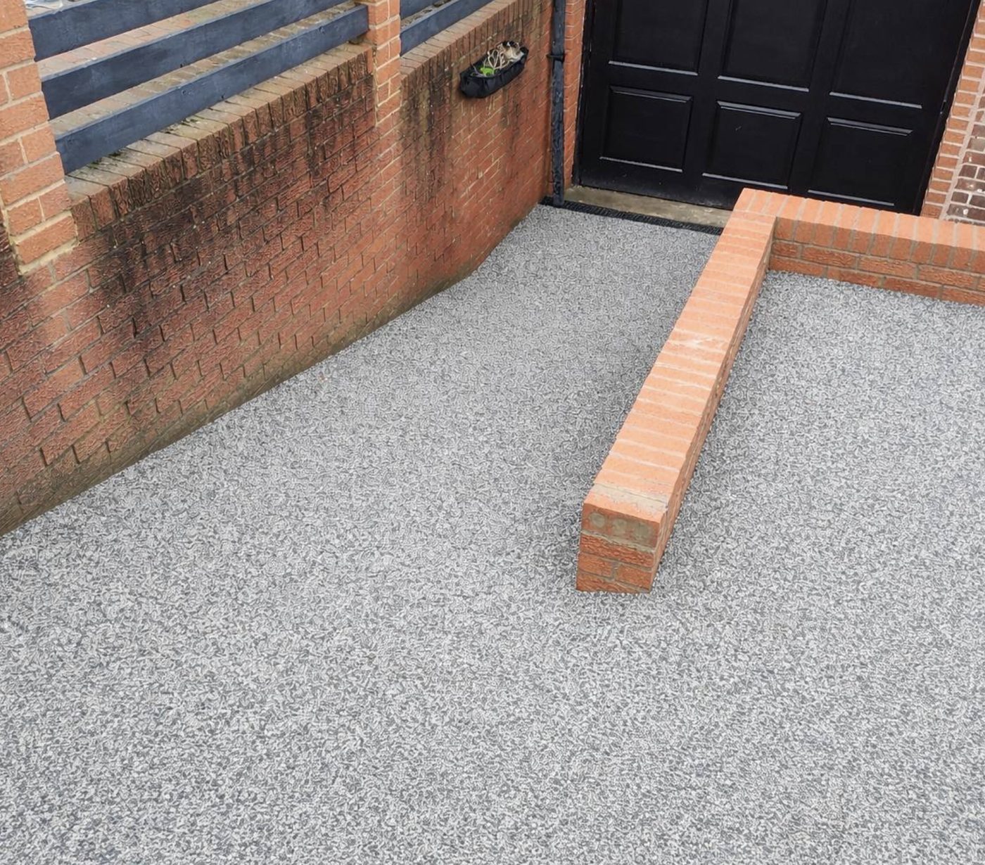 Grey resin driveway laid up to a brick wall and black garage doors