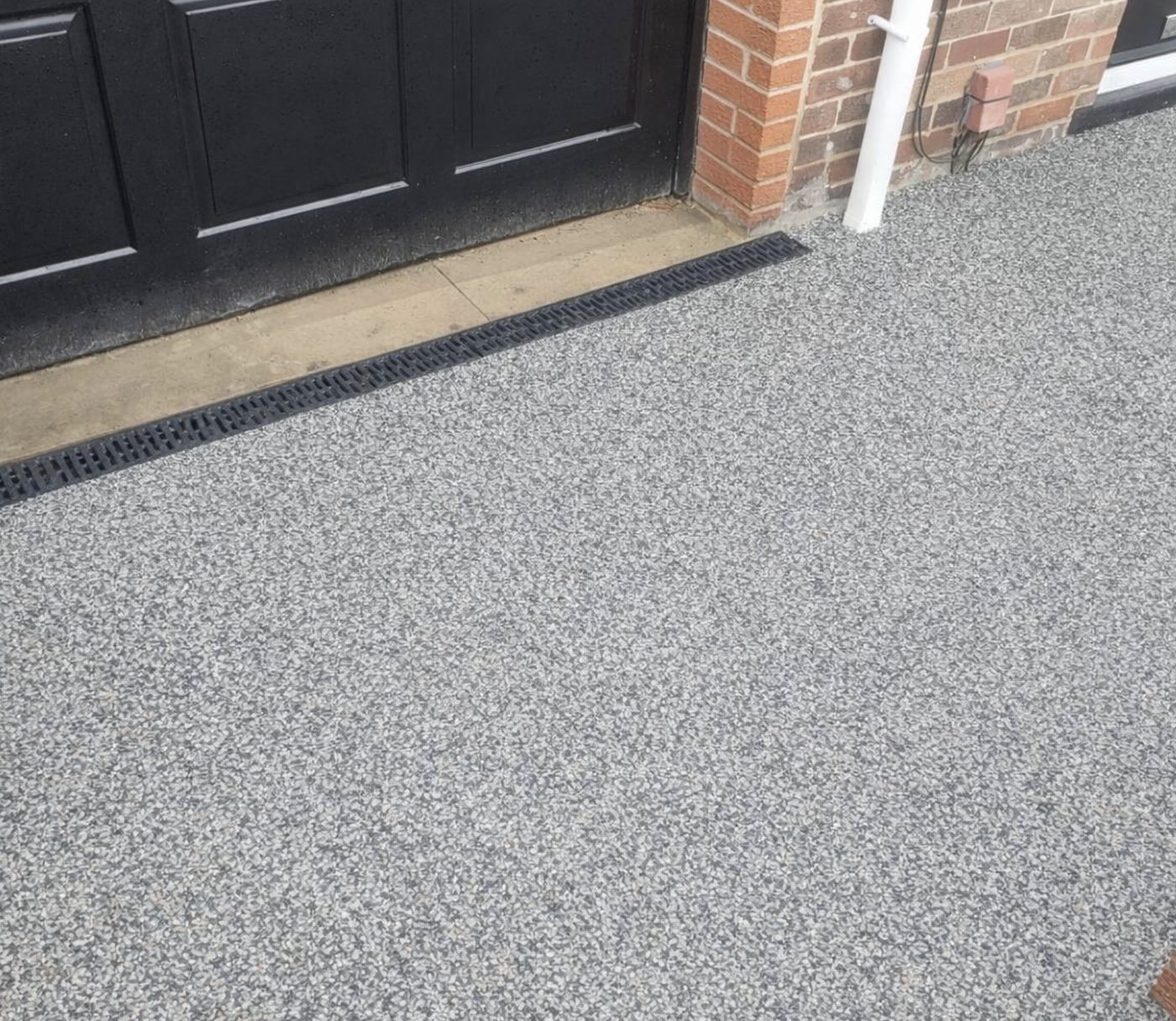 Resin driveway meeting a channel drain in front of a black garage door