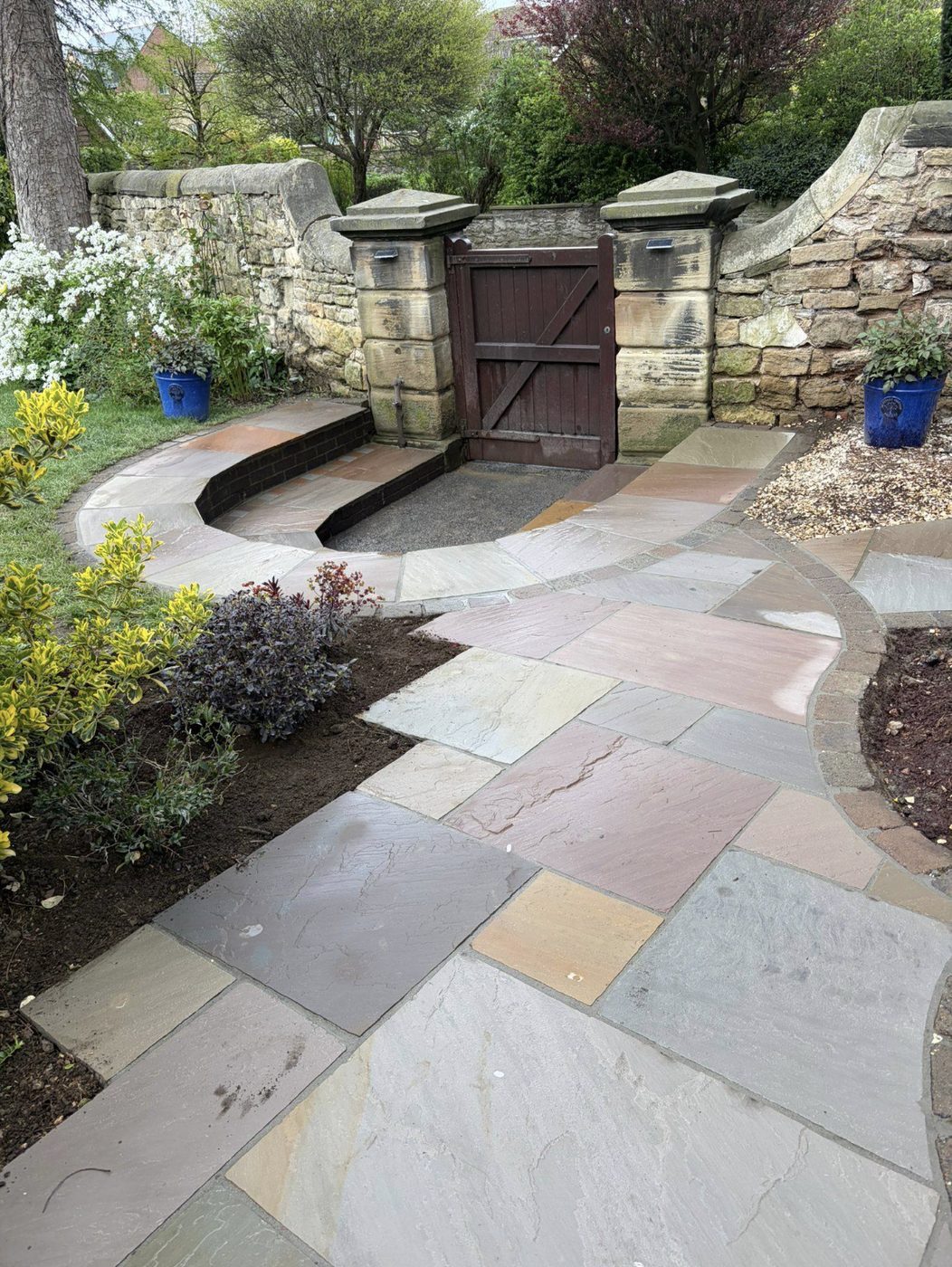 Sandstone path curving through a stone-walled garden to a timber gate between stone gate posts
