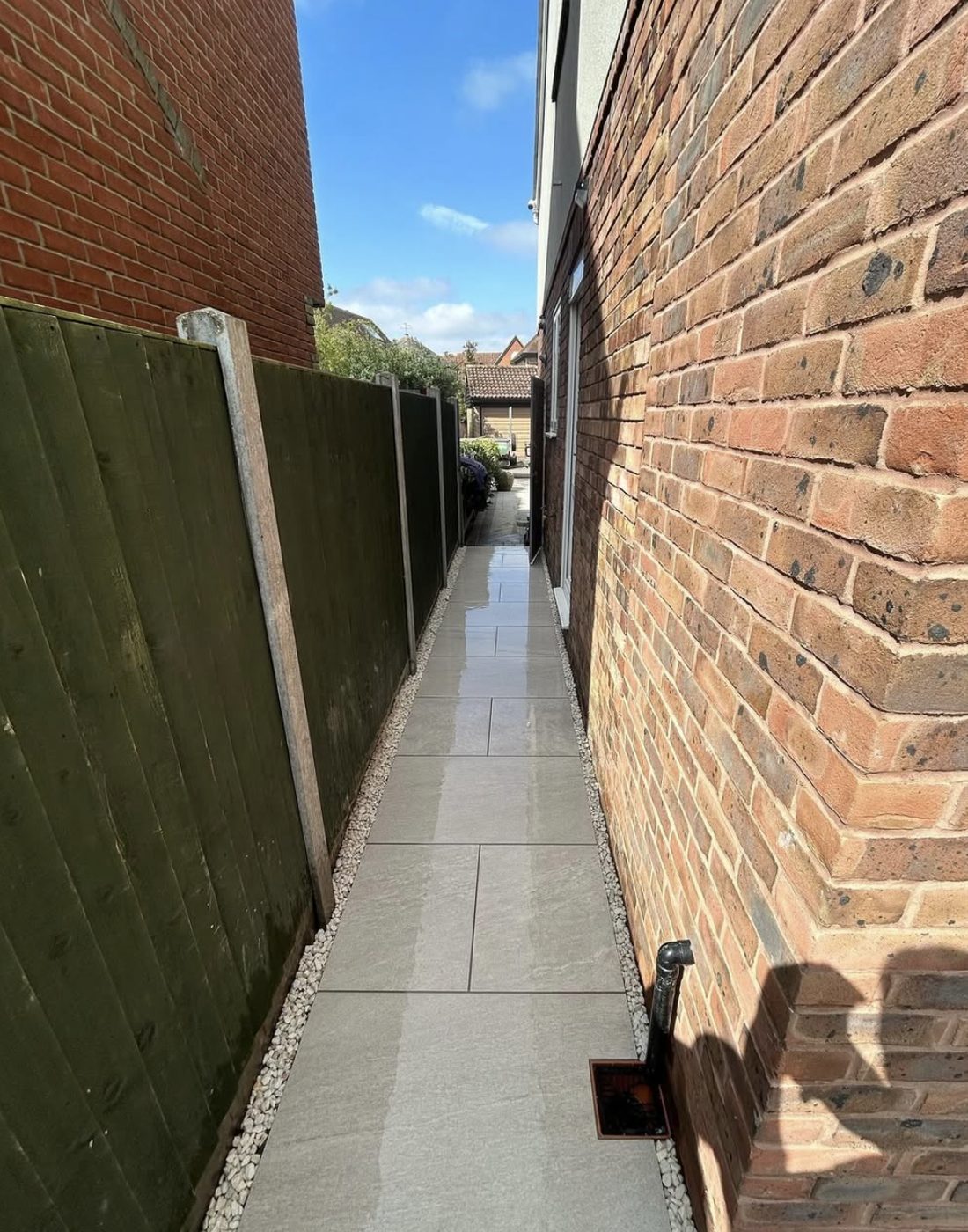 Narrow porcelain side path running between a brick house and a fence with white pebble margins